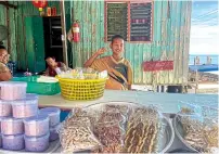  ??  ?? A boy helps his parents sell sun-dried fish and squid in front of their house on Koh Raet. The dried seafood and kapi (shrimp paste) are popular goods from the island. The shop also sells shells, the by-products of their daily catch.