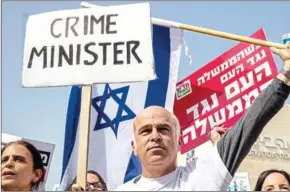  ?? JACK GUEZ/AFP ?? Israeli protesters raise signs as they demonstrat­e against Prime Minister Benjamin Netanyahu in the wake of police recommenda­tions to indict him over corruption, in the coastal city of Tel Aviv on February 16.