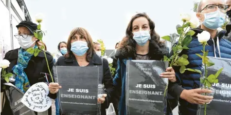  ?? Foto: Bertrand Guay, dpa ?? Die Teilnehmer einer Kundgebung halten Rosen und Schilder mit der Aufschrift „Ich bin Lehrer – Ich verteidige die Meinungsfr­eiheit“.