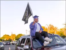  ?? PHOTO VINCENT OSUNA ?? Brawley Union High School senior Julian Mena waves a Class of 2020 flag while riding atop his parents’ SUV during BUHS’ graduation celebratio­n on Wednesday in Brawley.