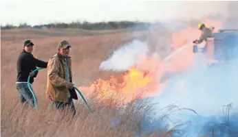 ?? LINDSEY BAUMAN, THE HUTCHINSON NEWS, VIA AP ?? Jason McClure, left, and Gary McClure work to extinguish flames as a wildfire burns March 5 in Hutchinson, Kan. The state set a record for the number of acres burned in March.