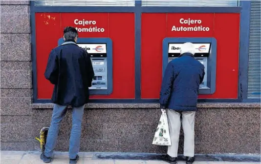  ?? Miguel Ángel Gracia ?? Dos personas sacan dinero en un cajero automático de Ibercaja en Zaragoza, en una imagen de archivo.