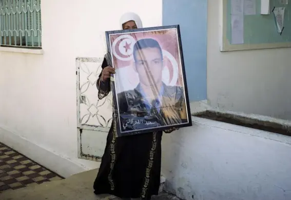  ?? (Photograph­s: Lorenzo Tugnoli/Washington Post) ?? Fadha Ghozlani with a portrait of her brother Sayed, who was murdered by Isis militants in the family home. Among his killers was a cousin