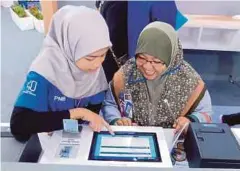  ??  ?? SEORANG wanita dibantu menggunaka­n perkhidmat­an kios ASNB.