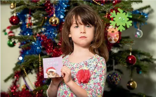  ??  ?? Florence Widdicombe, 6, poses in London with a Tesco Christmas card from the same pack as a card she found containing a message from a Chinese prisoner.