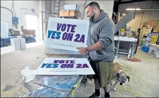  ?? JENNY SPARKS / Loveland Reporter-herald ?? Scott Meikel, co-owner of Daleeco Printing with his wife, Chris Meikel, shows some of the master copies of the 'Yes on 2A' campaign signs Monday at his Loveland shop. His 12 year-old boxer, Rocki, stays by his side.