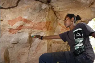  ??  ?? Daluk (woman) ranger Annemarie Ahwon holds a colour scale by a reclining figure at Marebu, near Manmoyi. Rangers photograph all rock art with and without technical details to ensure they are documented and recorded accurately.