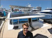  ??  ?? Michael Kohler, CEO of Austria-based Solarwave Yachts, stands aboard his solar-powered yacht at the boat show. Solar panels that line the boat’s upper decks soak up enough power to cross an ocean.