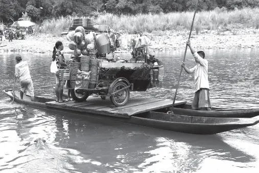  ?? PNA photo ?? BOATMEN paddle an improvised raft, the only means to transport a tricycle loaded with merchandis­e goods, across the river in Barangay Daraitan, Tanay, Rizal. Meanwhile, a dog seemingly enjoys a dip as it swims in the river.