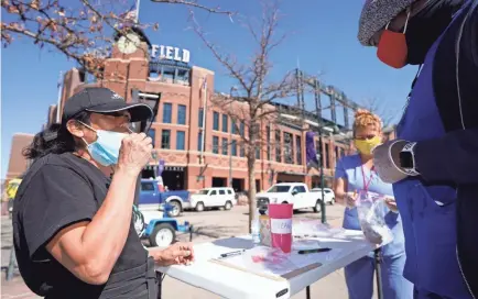  ?? DAVID ZALUBOWSKI/AP ?? Martha Bravo, left, self-administer­s a swab coronaviru­s test under the guidance of Josh Copeland at a table set up outside Coors Field as fans return for a baseball game April 1 in Denver.