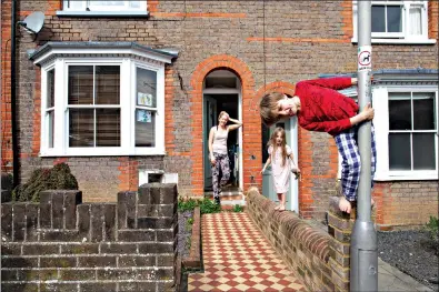  ?? AP Photo/Elizabeth Dalziel ?? Jude 5, and Zofia 4, play in their pajamas outside their home while their mom, Katharine, looks out from their doorway while on lockdown April 8 in Berkhamste­d, England. Katharine was furloughed and has taken advantage of the extra time her leave from work has given her. She contacted "Safer Places," a women's refuge from domestic violence, and has organized donations to the organizati­on from her neighbors.