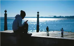  ?? ARMANDO FRANCA/AP ?? A young man checks his phone Jan. 30 by the Tagus River in Portugal.