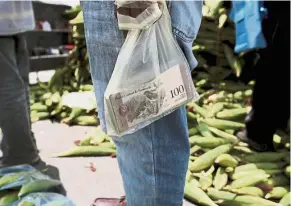  ??  ?? The little that’s left: A vendor holding bank notes in a plastic bag at a market in Caracas. — AP