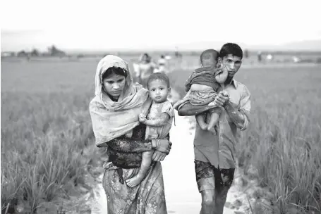  ?? Associated Press ?? n Myanmar’s Rohingya ethnic minority members walk through rice fields Friday after crossing over to the Bangladesh side of the border near Cox’s Bazar’s Teknaf area. Myanmar’s military says almost 400 people have died in recent violence in the western...