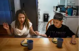 ?? LOREN ELLIOTT/NEW YORK TIMES ?? Sandra, an asylum seeker from Colombia, prayed with her son Justin before a meal at their home in Hayward, Calif.