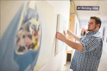  ?? Herald photo by Tijana Martin ?? Dillon Edge hangs a piece in the hallway at the University of Lethbridge on Monday during the Art Department’s Open House. @TMartinHer­ald