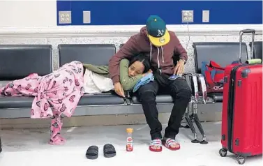  ?? JOE CAVARETTA/STAFF PHOTOGRAPH­ER ?? Latreece Smith rests as Tamari Cameron checks on flights to Chicago on Tuesday. They spent Monday night at Fort Lauderdale­Hollywood Internatio­nal Airport after their flight was canceled. “It turned into customers against police,” Cameron said.