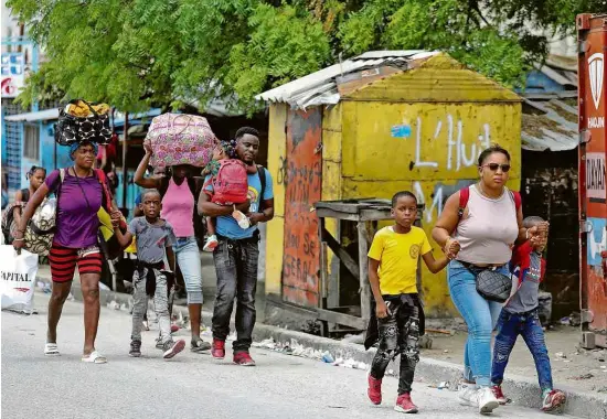  ?? Ralph Tedy Erol - 2.mai.22/Reuters ?? Haitianos carregam seus pertences ao fugir de embates entre gangues em Porto Príncipe