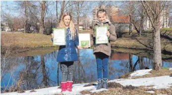  ?? FOTO: TOBIAS SCHUMACHER ?? Greta Hege (links) und Mirja Schättiger mit ihrem Naturtageb­uch und den Urkunden an ihrem „Forschungs­weiher“an der Birkenalle­e im Rotmoos.