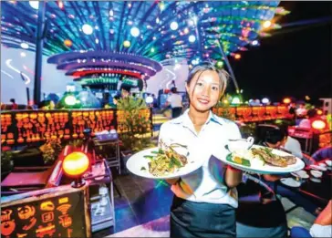  ?? HONG MENEA ?? A staff member shows off a signature dish before serving customers at The Moon Sky Bar in Siem Reap as its peacock decoration is seen in the background.