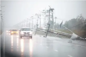  ??  ?? Cars and fallen electricit­y poles are seen along a road. — Reuters photo