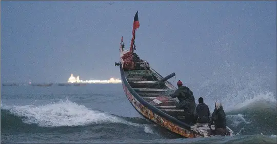  ?? ?? Fishermen on a traditiona­l boat known as pirogue leap over a wave Jan. 18 while heading out to the Atlantic Ocean as an offshore gas terminal is seen at the horizon in Saint Louis.