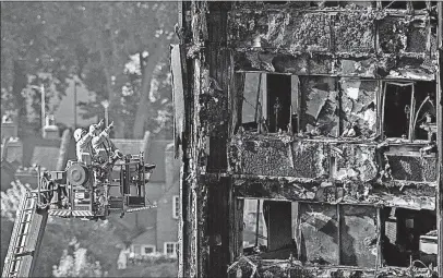  ?? [RICK FINDLER/PRESS ASSOCIATIO­N] ?? Firefighte­rs survey the damage to the fire-gutted Grenfell Tower in London. Two British government officials said Sunday the cladding used on the facade in a renovation of Grenfell Tower might have been banned under building regulation­s. The cladding...