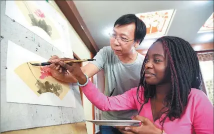  ?? XINHUA ?? An African student from the Confucius Institute at the University of Zambia uses a brush to create a Chinese painting under the guidance of an art teacher at the Shijiazhua­ng No 42 Middle School, also called Hebei Internatio­nal School. She is part of a...