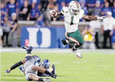  ?? GERRY BROOME/AP ?? Hurricanes running back Mark Walton leaps over Duke defenders Ben Humphreys and Bryon Fields Jr. during the first half.