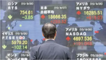  ?? — Reuters ?? A pedestrian looks at electric boards displaying Tokyo’s Nikkei Stock Average in Tokyo, Japan.