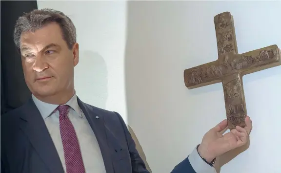  ??  ?? Il gesto Il ministro presidente bavarese Markus Söder, 51 anni, appende una croce all’ingresso della cancelleri­a della Baviera dopo aver annunciato il provvedime­nto che obbliga a tenerne una in ogni ufficio pubblico
