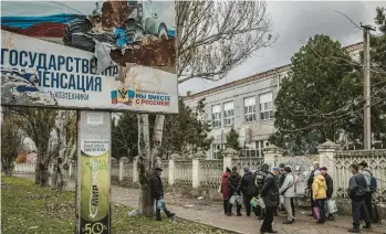  ?? FINBARR O’REILLY/THE NEW YORK TIMES ?? Ukrainians line up to get water near a torn Russian propaganda sign Nov. 16 in Kherson.