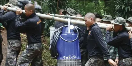 ??  ?? Soldiers carry a pump to help drain the rising flood water in a cave where 12 boys and their soccer coach have been trapped since June 23, in Mae Sai, Chiang Rai province, in northern Thailand on Friday. Thai authoritie­s are racing to pump out water...