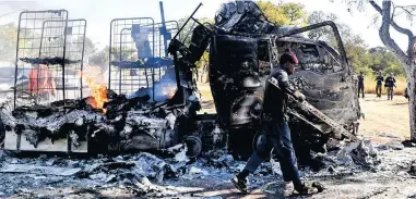  ?? PICTURE: AP ?? VIOLENCE: A man carries metal from a burnt truck on a road in Atteridgev­ille, Pretoria, yesterday.