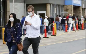  ?? DAVE SCHERBENCO — THE CITIZENS’ VOICE VIA AP ?? A couple walks by a long line of shoppers waiting for their chance to get into a Walmart on Saturday in Wilkes-Barre, Pa., as the businesses begins limiting the amount of customers in the store due to the coronaviru­s.