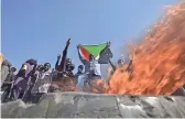  ?? AFP VIA GETTY IMAGES ?? A man holds a Sudanese national flag in front of flames at a barricade as people protest against the military coup in Sudan.