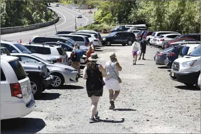  ?? The Maui News MATTHEW THAYER photo ?? Visitors to Twin Falls make their way across the parking lot Friday. In the background along Hana Highway is the overflow lot, which has been taken out of service while being used as a staging area for a bridge repair project 2 miles down the road. The limited parking has made an already crowded situation even more difficult.