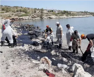  ??  ?? Workers try to clean up a beach on the island of Salamina, which has been hit by an oil slick after a small tanker went down near its coast on Sunday carrying 2,200 tons of fuel oil and 370 tons of marine gas oil.