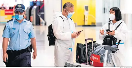  ?? JAMES GOURLEY / EFE ?? Dos sanitarios con un equipo de protección charlan ayer en presencia de un policía en el aeropuerto de Sidney.