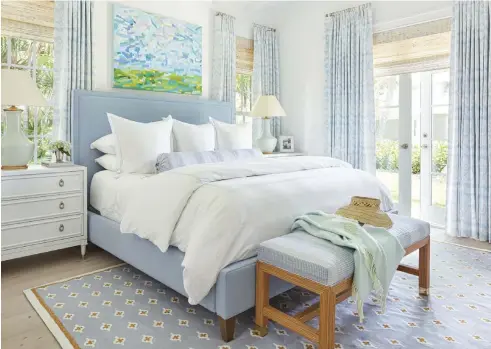  ?? ?? |BELOW| SEASIDE SERENITY. The primary bedroom looks as fresh as the nearby ocean. A beamed white ceiling frames the room’s linen-cotton blend draperies from Quadrille. The seascape art above the headboard was commission­ed from artist Lucy Williams. The area rug was custom designed for the room, which has a view of the front of the home.