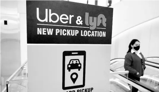  ?? AP ?? In this February 9, 2021 file photo, a woman walks past a sign offering directions to an Uber and Lyft ride pickup location at Logan Internatio­nal Airport, in Boston.