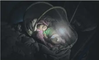  ??  ?? Abraha Kinfe Gebremaria­m uses a flashlight to check on his 4-month-old twin daughters Aden and Turfu after praying at a church early in the morning in Hamdayet, Sudan, near the border with Ethiopia.