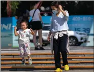  ?? (AP/Mark Schiefelbe­in) ?? A woman watches as a child jumps down some steps Saturday in Beijing.
