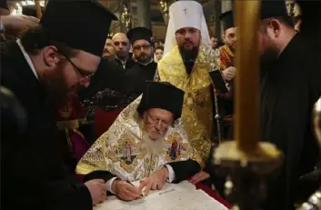  ?? Emrah Gurel/Associated Press ?? Ecumenical Patriarch Bartholome­w I, center, signs the “Tomos” decree of autocephal­y for the Ukrainian church as Metropolit­an Epiphanius, center right, the head of the independen­t Ukrainian Orthodox Church, watches Jan. 5 at the Patriarcha­l Church of St. George in Istanbul.