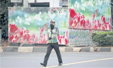  ?? REUTERS ?? An Indonesian police officer walks by a boarded up police box that was hit during Thursday’s gun and bomb attack in Jakarta, which killed seven people and injured 20.