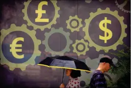  ?? ASSOCIATED PRESS ?? PEOPLE WALK PAST A MURAL DISPLAYING WORLD CURRENCY SYMBOLS on the outside of a bank in Beijing on Friday. China’s central bank is allowing its tightly controlled yuan to drift lower against the dollar, a move that could help exporters cope with U.S. tariff hikes but raises the risk of reigniting an outflow of capital Beijing spent months trying to stanch.