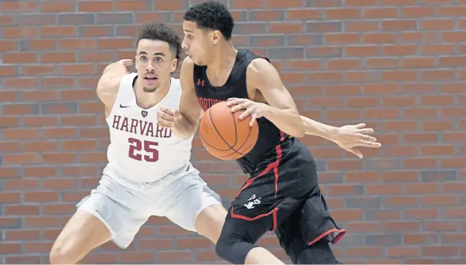  ?? JIM MICHAUD / BOSTON HERALD ?? IN THE ZONE: Jordan Roland (right) drives past Corey Johnson for two of his career-high 34 points in Northeaste­rn’s 81-71 win against Harvard last night at Lavietes Pavilion. The Huskies evened their record at 1-1 after an opening night loss to Boston University.