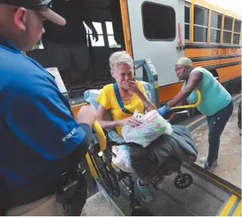  ?? AP PHOTOS ?? Above, Glynn County school resource officer Mark Hooper, left, and school support staff member Sheree Armstrong, right, help Elizabeth Scales board a special needs bus Monday at Lanier Plaza in Brunswick, Ga. as hundreds of local residents evacuate the area Monday under mandatory evacuation ahead of Hurricane Dorian.