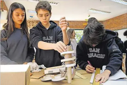  ??  ?? FÓRMULA B. Los estudiante­s preparan una pista de cartón para bolitas en la que medirán las fuerzas, velocidad, distancia y rozamiento.