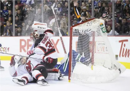 ??  ?? VANCOUVER: Vancouver Canucks’ Adam Cracknell crashes into New Jersey Devils goalie Cory Schneider and the net after being taken down by Devils’ Adam Larsson, front, of Sweden, during the first period of an NHL hockey game in Vancouver, British...